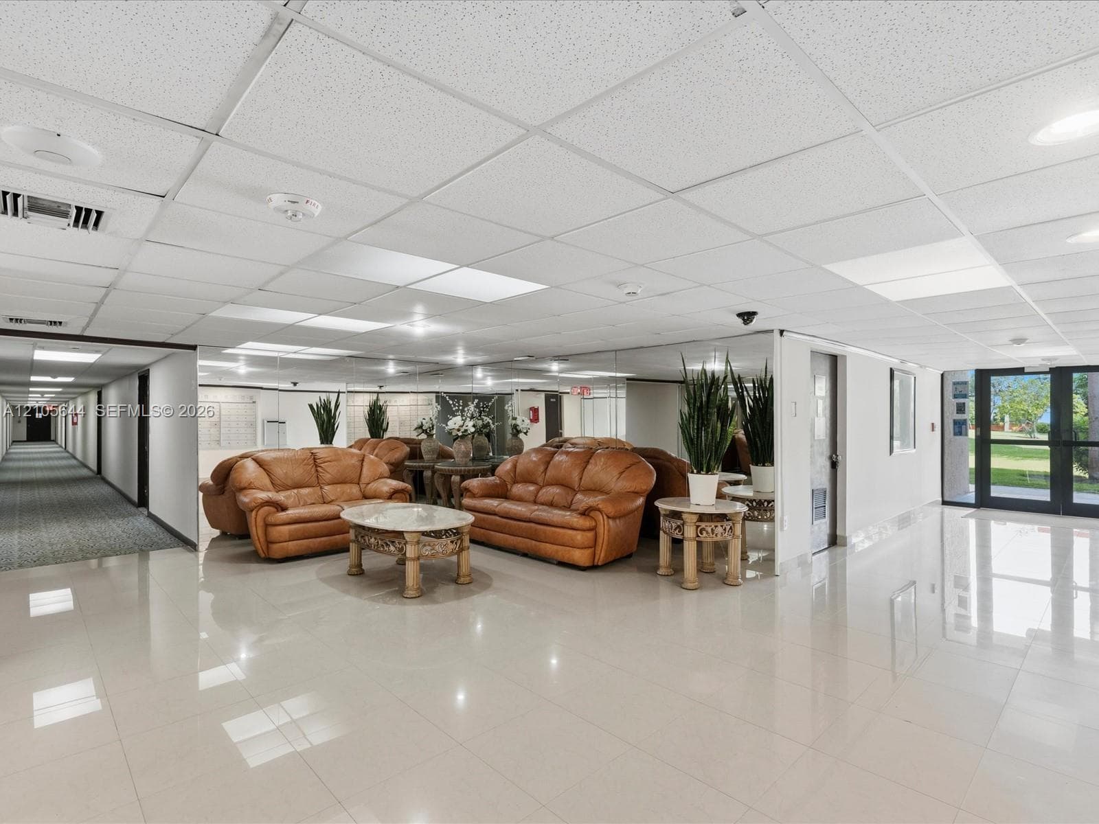 Common area featuring large-format ceramic tile flooring, a suspended acoustic tile ceiling with integrated recessed lighting, and expansive wall-to-wall mirrors