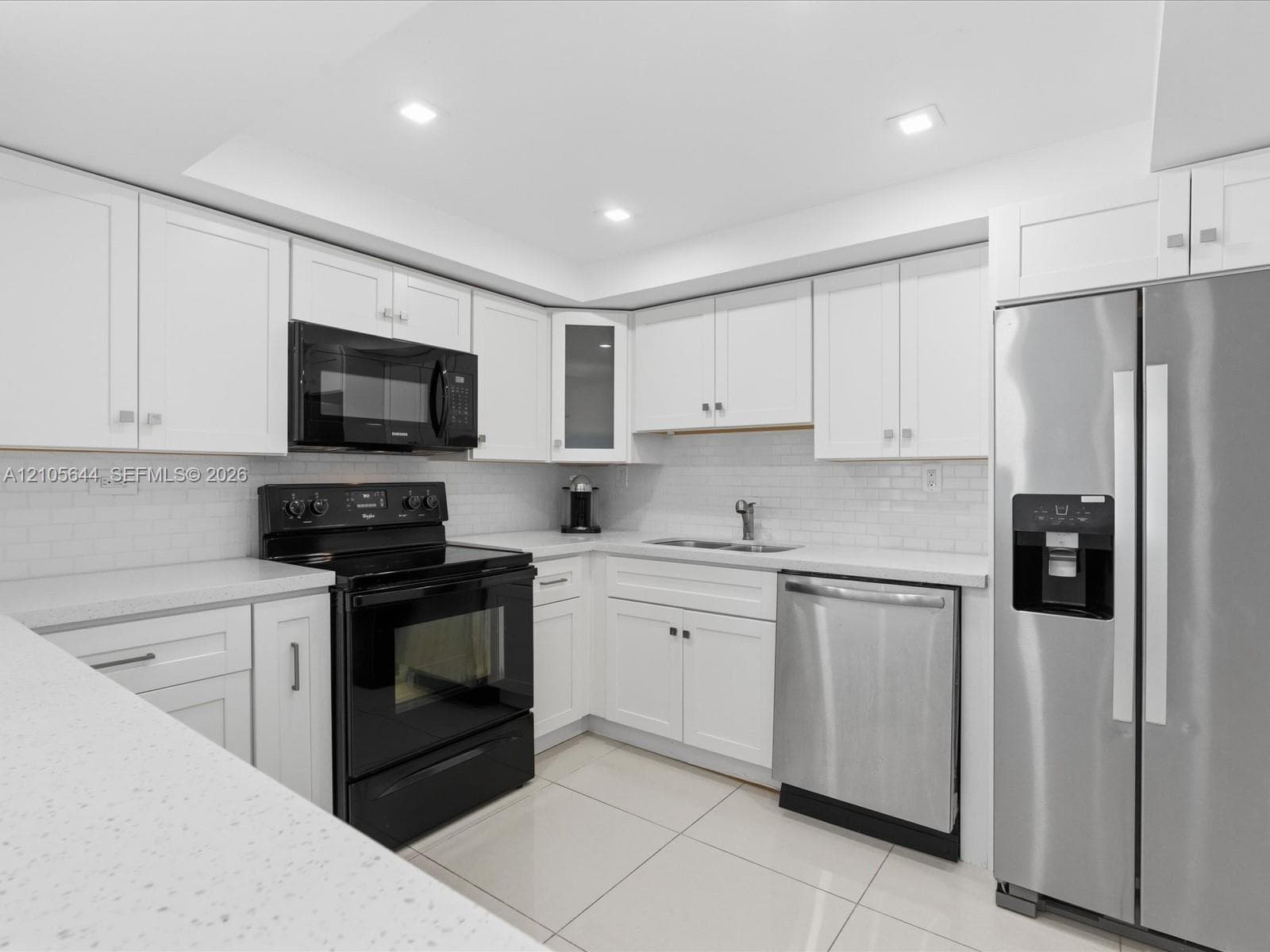 Kitchen featuring white shaker-style cabinetry, solid-surface countertops, a subway tile backsplash, recessed lighting, and stainless steel and black appliances