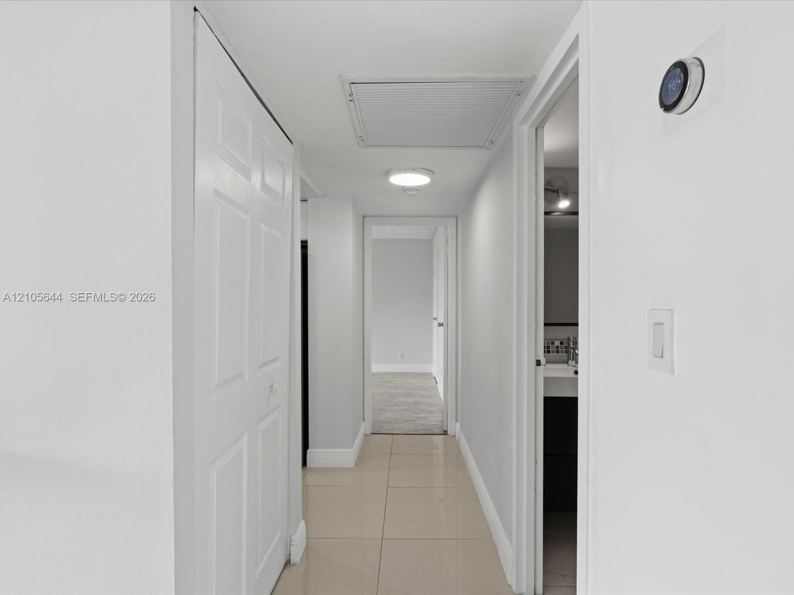 Hallway featuring large-format ceramic tile flooring, double-panel closet doors, ceiling-mounted light fixture, and smart thermostat