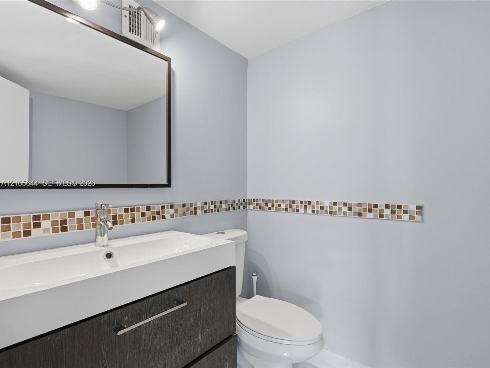 Floating vanity with integrated sink, rectangular framed mirror, chrome fixtures, and mosaic tile wall accent