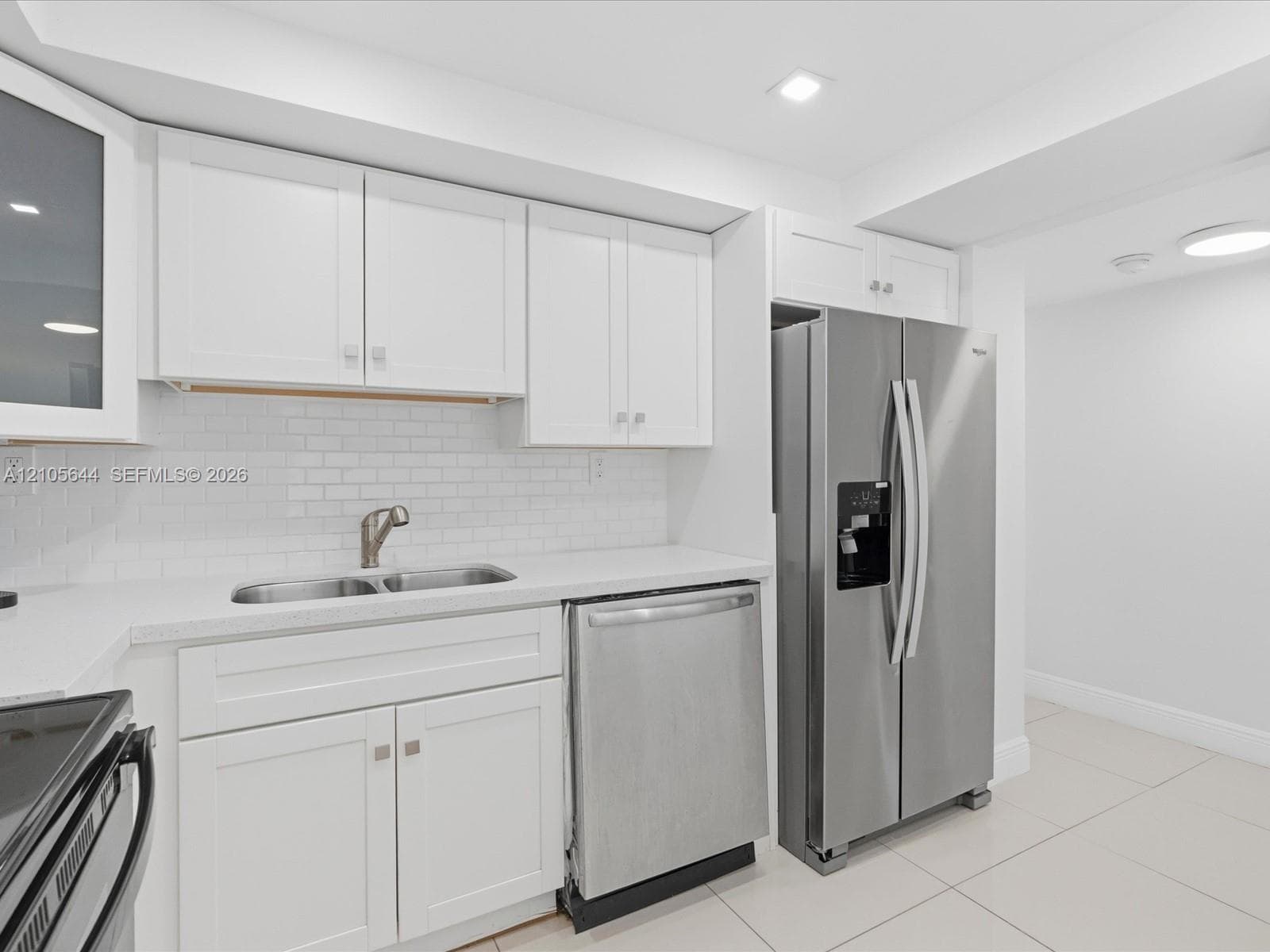 Kitchen featuring white shaker-style cabinetry, a white subway tile backsplash, stainless steel appliances, a double-basin sink, and tile flooring