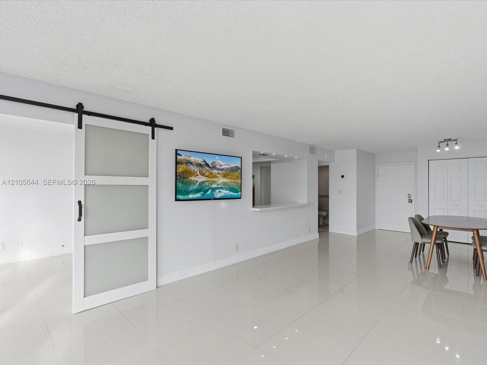 Open interior space featuring large-format tile flooring, a sliding barn-style door with frosted glass panels, a passthrough window with a ledge, and recessed lighting