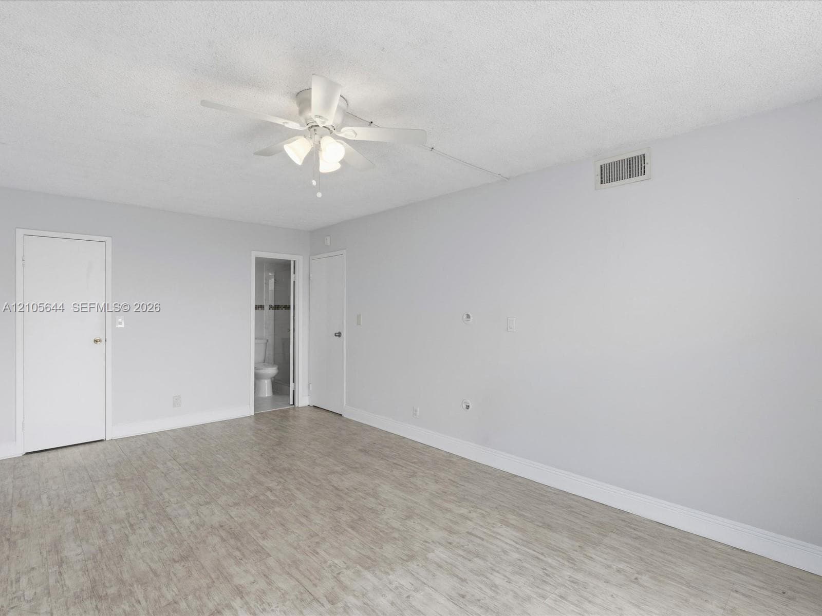 Neutral-toned room featuring wood-finish flooring, a central ceiling fan with integrated lighting, and multiple interior doors
