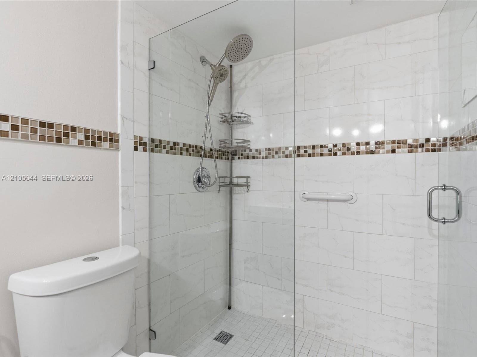 Walk-in shower featuring large-format white tile, glass enclosure, mosaic tile border, handheld shower fixture, and integrated grab bar