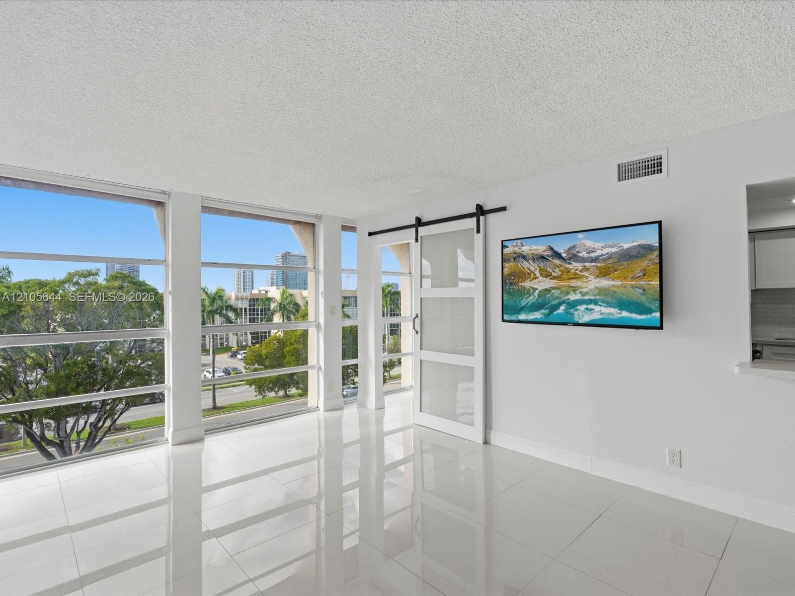 Floor-to-ceiling windows, white tile flooring, and a sliding glass barn door with a black metal track system