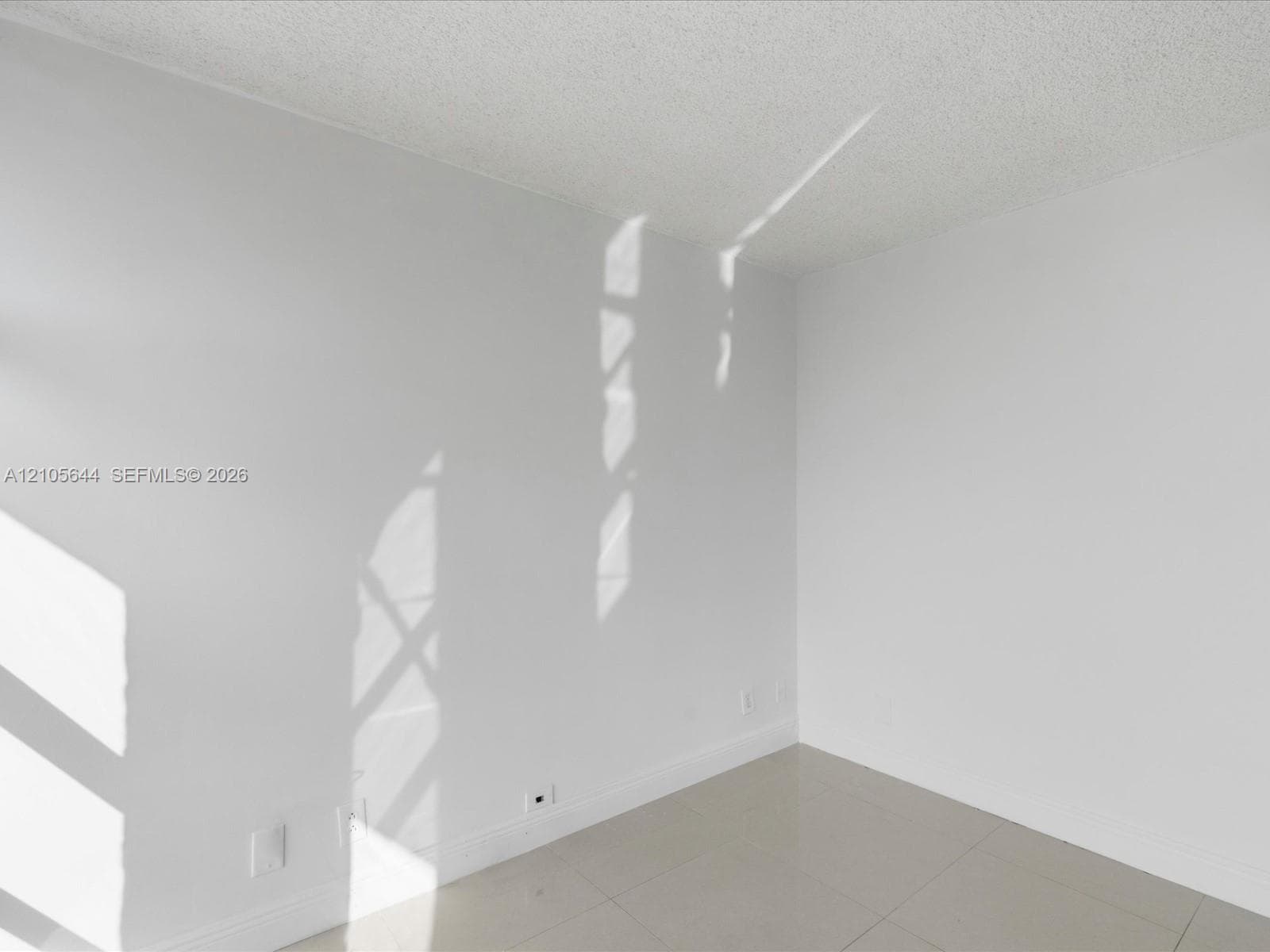 Neutral-toned interior space featuring light-colored tile flooring, smooth-finish walls, and a textured ceiling