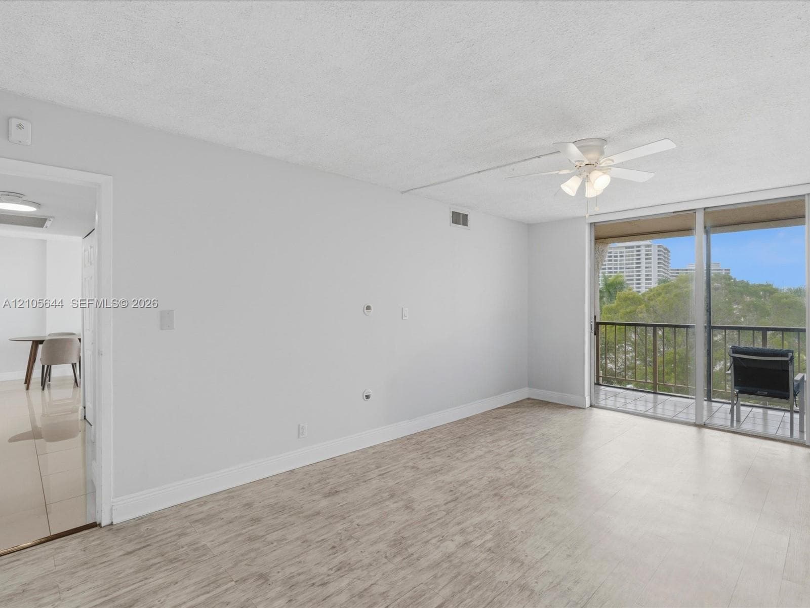 Living area featuring wood-finish flooring, a ceiling fan with integrated lighting, and sliding glass doors opening to a balcony with metal railings