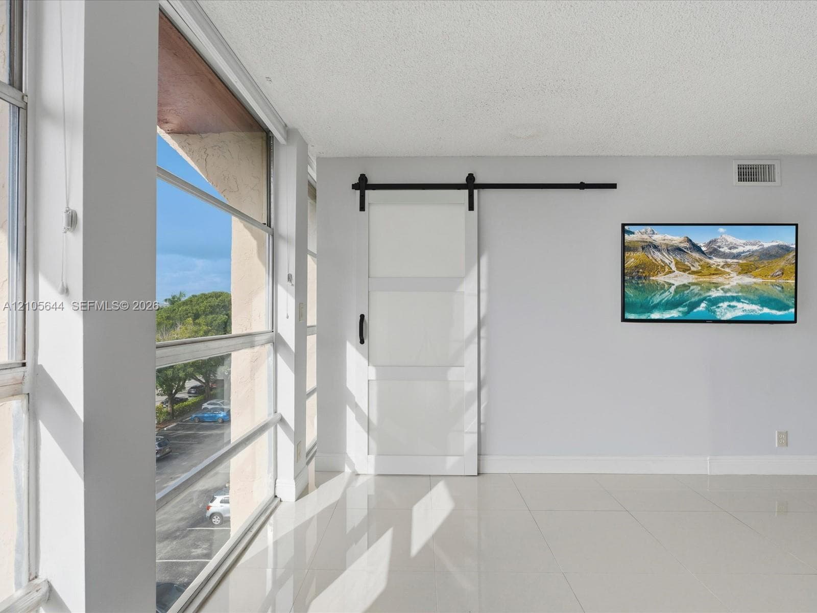 Large floor-to-ceiling windows, white tile flooring, and a white sliding barn door featuring matte black hardware