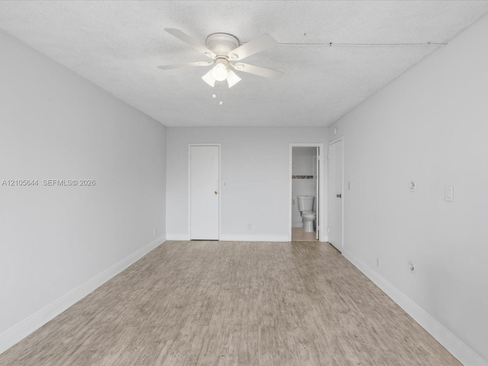 Neutral wall tones paired with wood-finish flooring and a multi-blade ceiling fan featuring integrated lighting