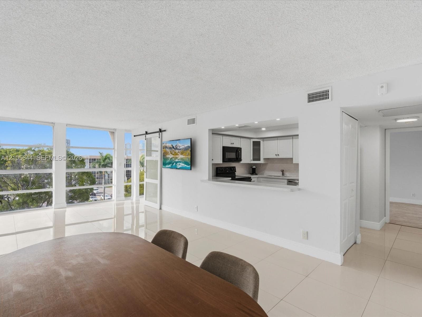 Large floor-to-ceiling windows, porcelain tile flooring, kitchen pass-through with breakfast bar, and sliding barn-style door