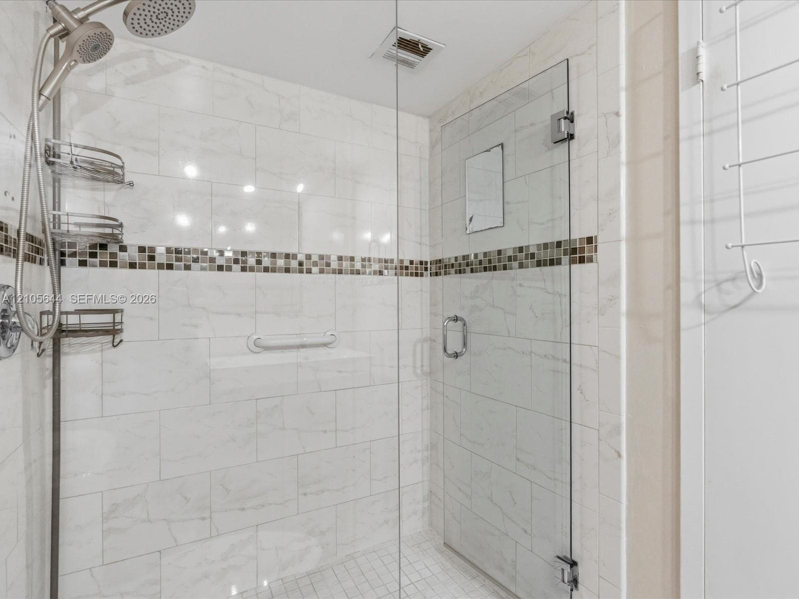 Walk-in shower featuring floor-to-ceiling large-format tile, mosaic accent band, glass panel enclosure, and handheld shower fixture