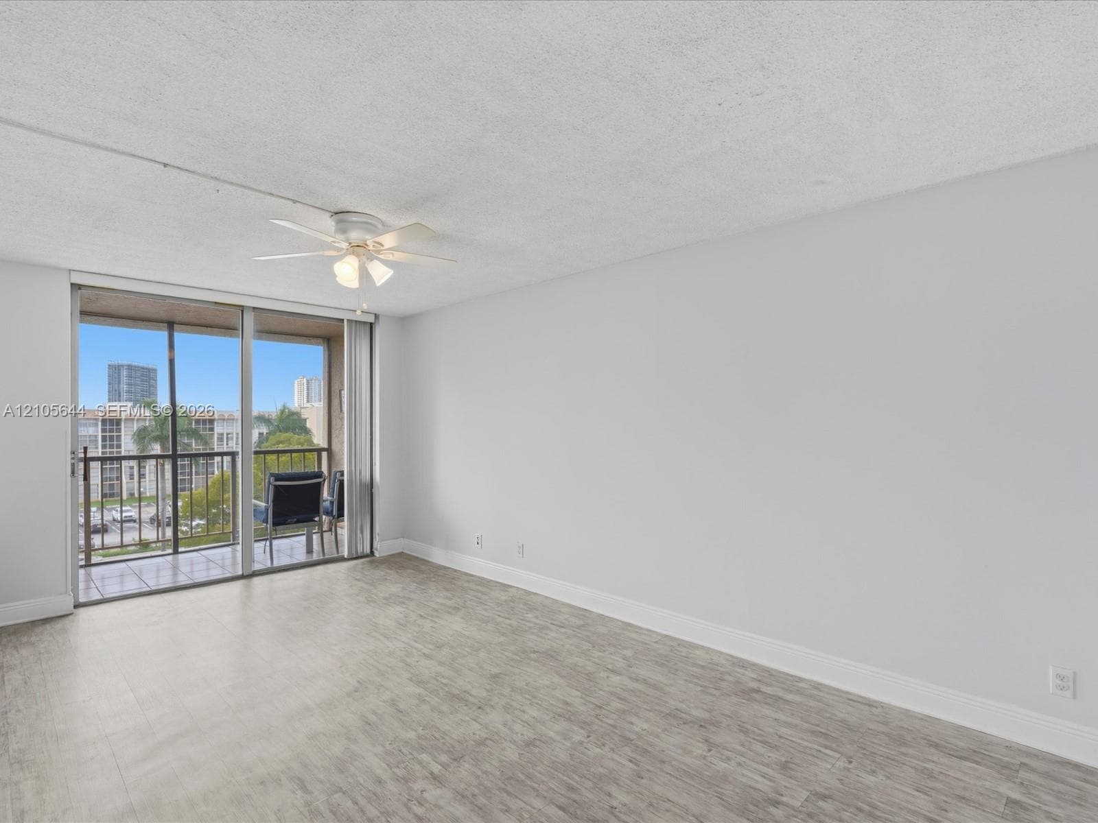 Neutral interior featuring wood-finish flooring, a ceiling-mounted light fixture with fan, and a floor-to-ceiling glass sliding door providing exterior access to a private balcony