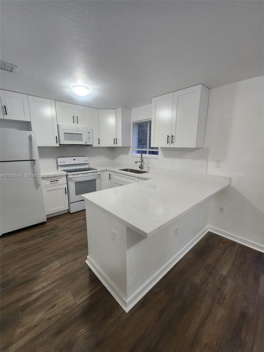 Kitchen featuring white shaker-style cabinetry, a peninsula with stone-finish countertops, wood-finish flooring, and a stainless steel under-mount sink with a chrome faucet