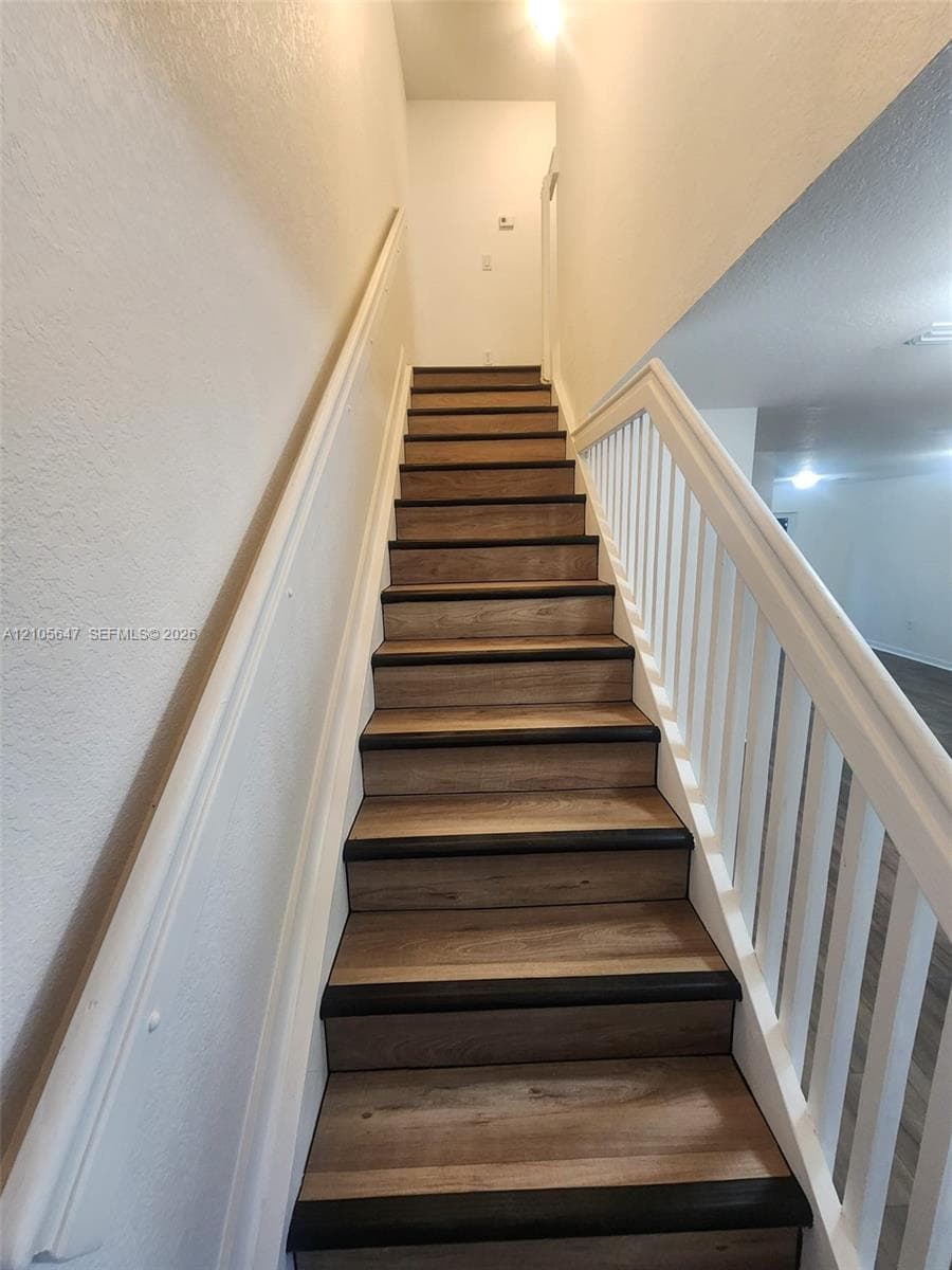 Staircase featuring wood-finish treads, dark-toned bullnose edges, white vertical balusters, and a matching white handrail