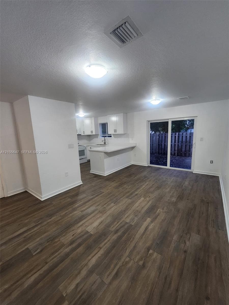 Open-concept interior featuring wood-finish flooring, white cabinetry, a breakfast bar, and glass sliding doors