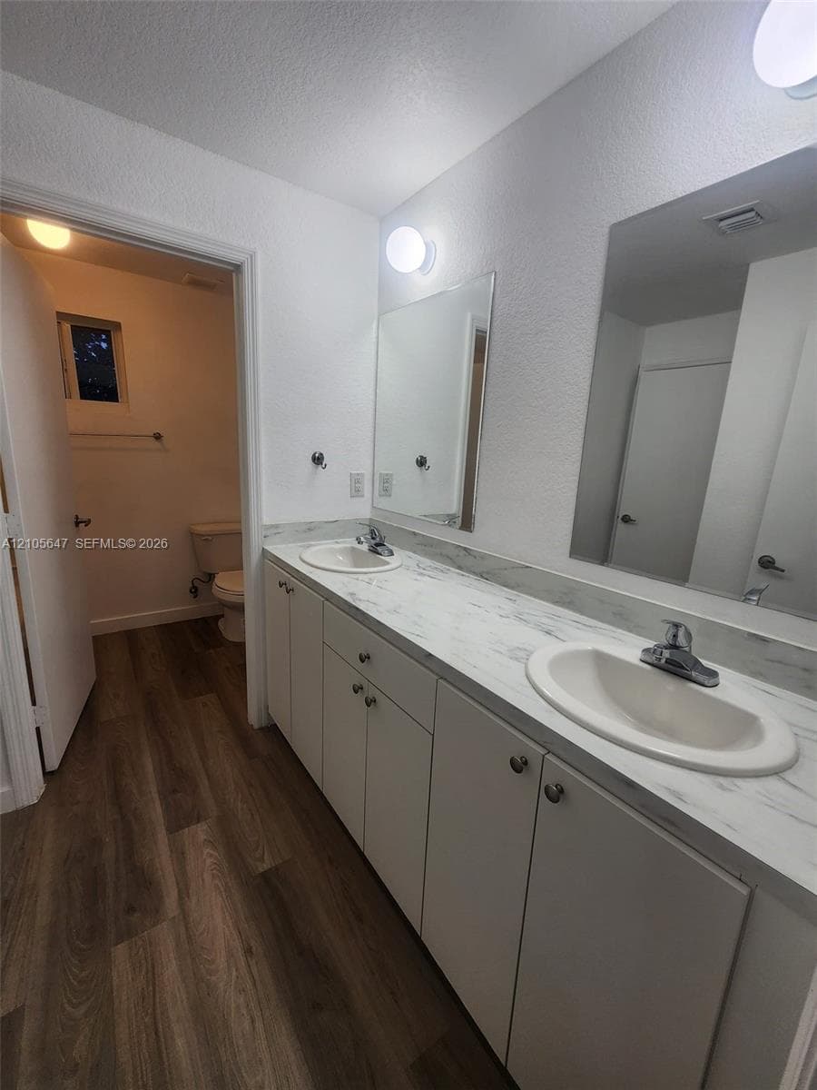Double vanity featuring a stone-look countertop, dual undermount oval sinks, chrome hardware, two wall-mounted mirrors, and wood-finish flooring