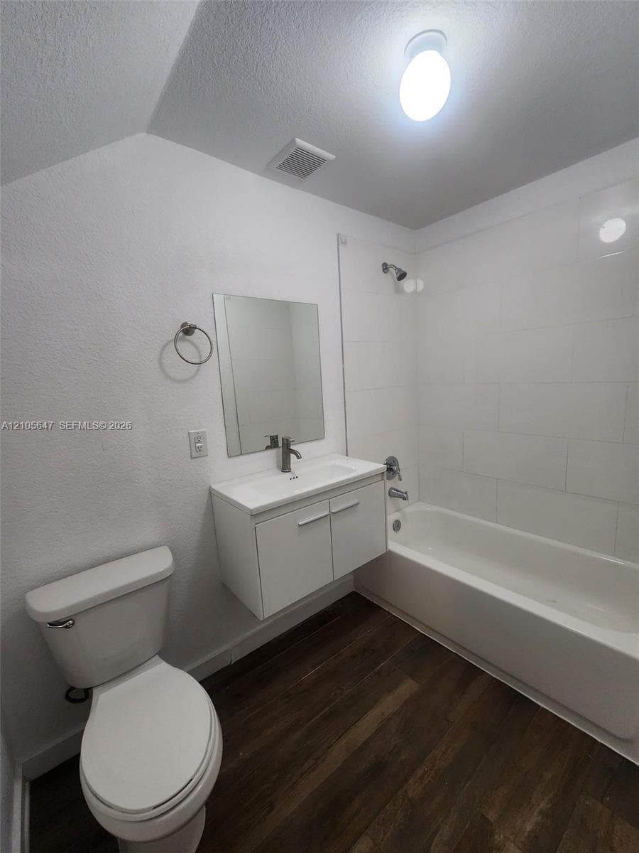Bathroom featuring a floating vanity with a white rectangular sink, white subway tile shower surround, chrome faucet, and wood-finish flooring