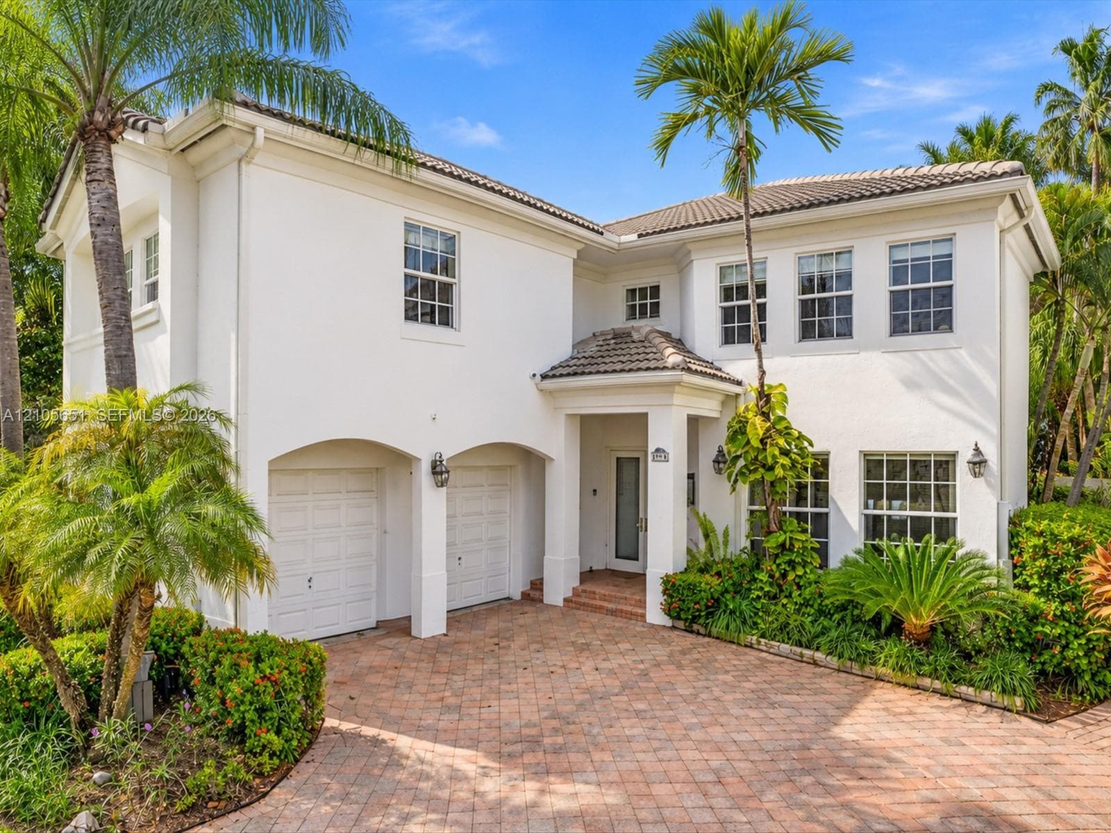Two-story stucco exterior featuring a covered entryway, multi-pane windows, a tiled roof, and a paved brick driveway with an integrated two-car garage