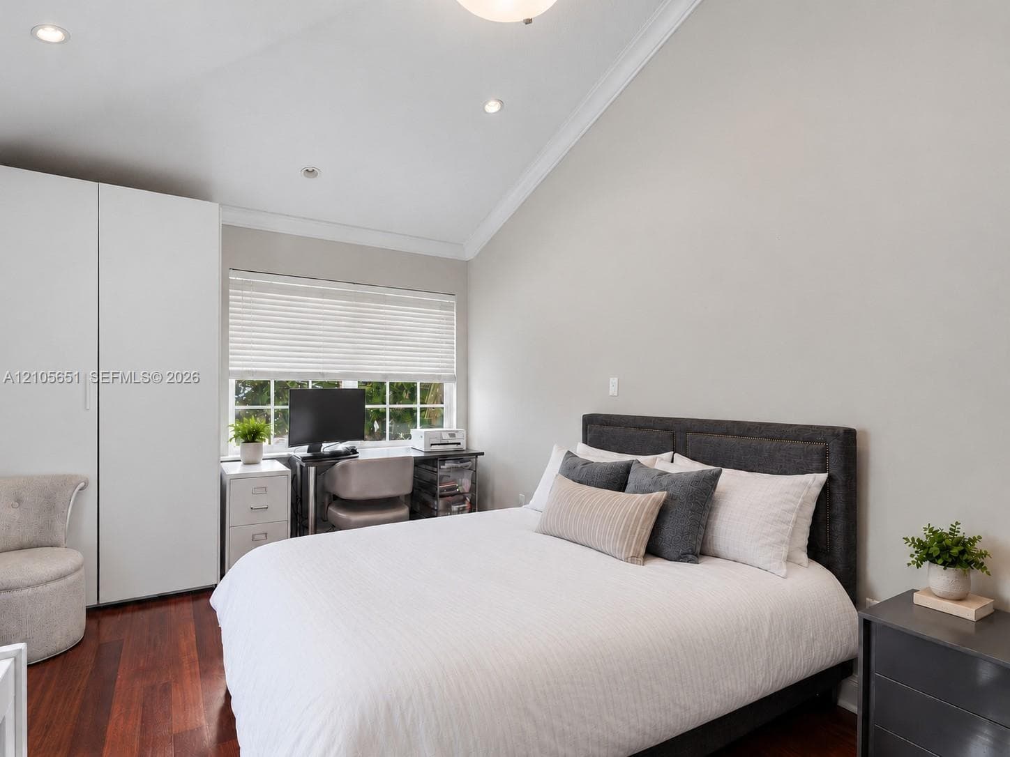 Vaulted ceiling, wood-finish flooring, multi-pane window with integrated blinds, and full-height built-in wardrobe cabinetry with matte finish