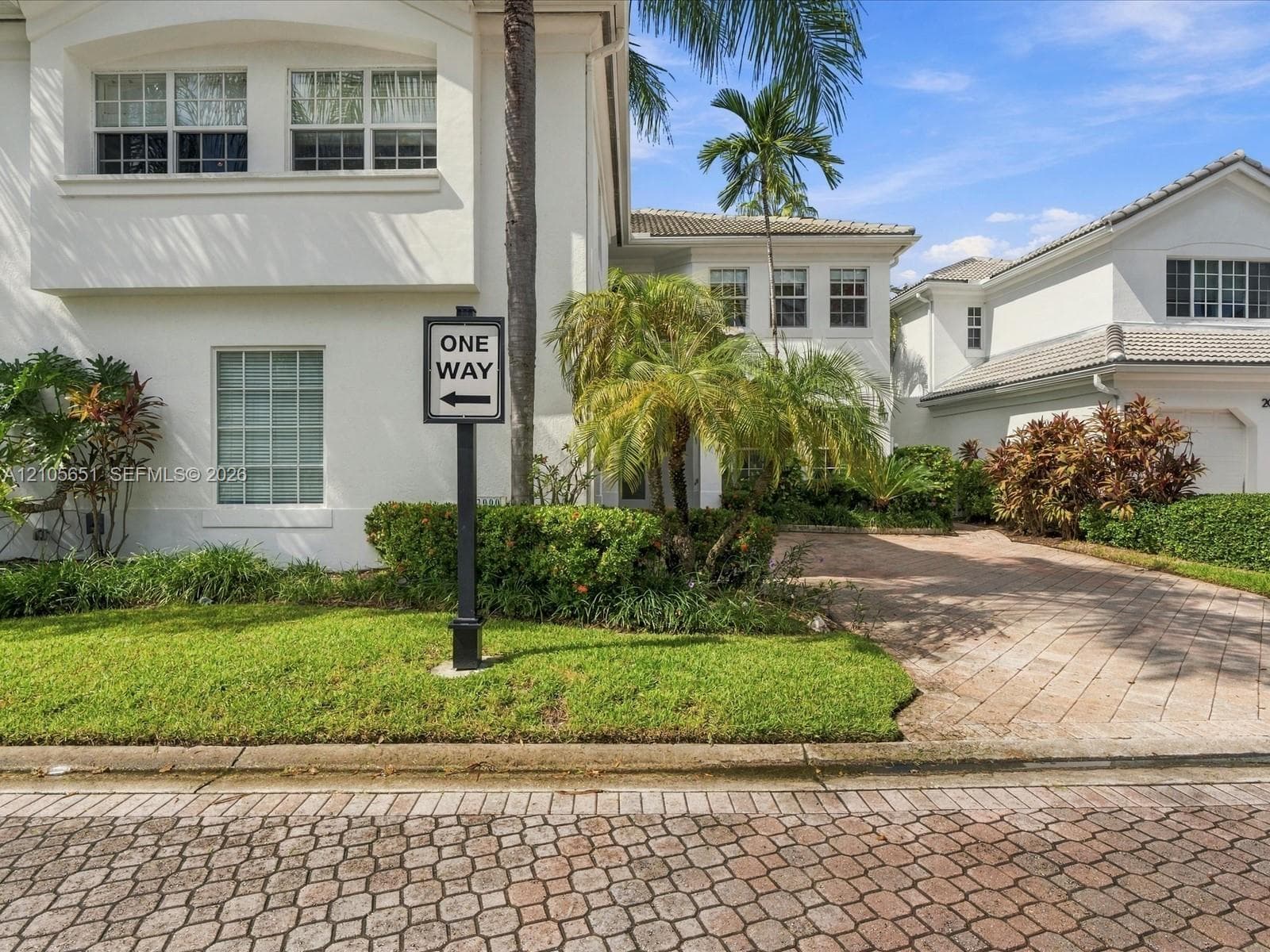 Stucco exterior featuring multi-pane windows, a tiled roof, and a paved brick driveway