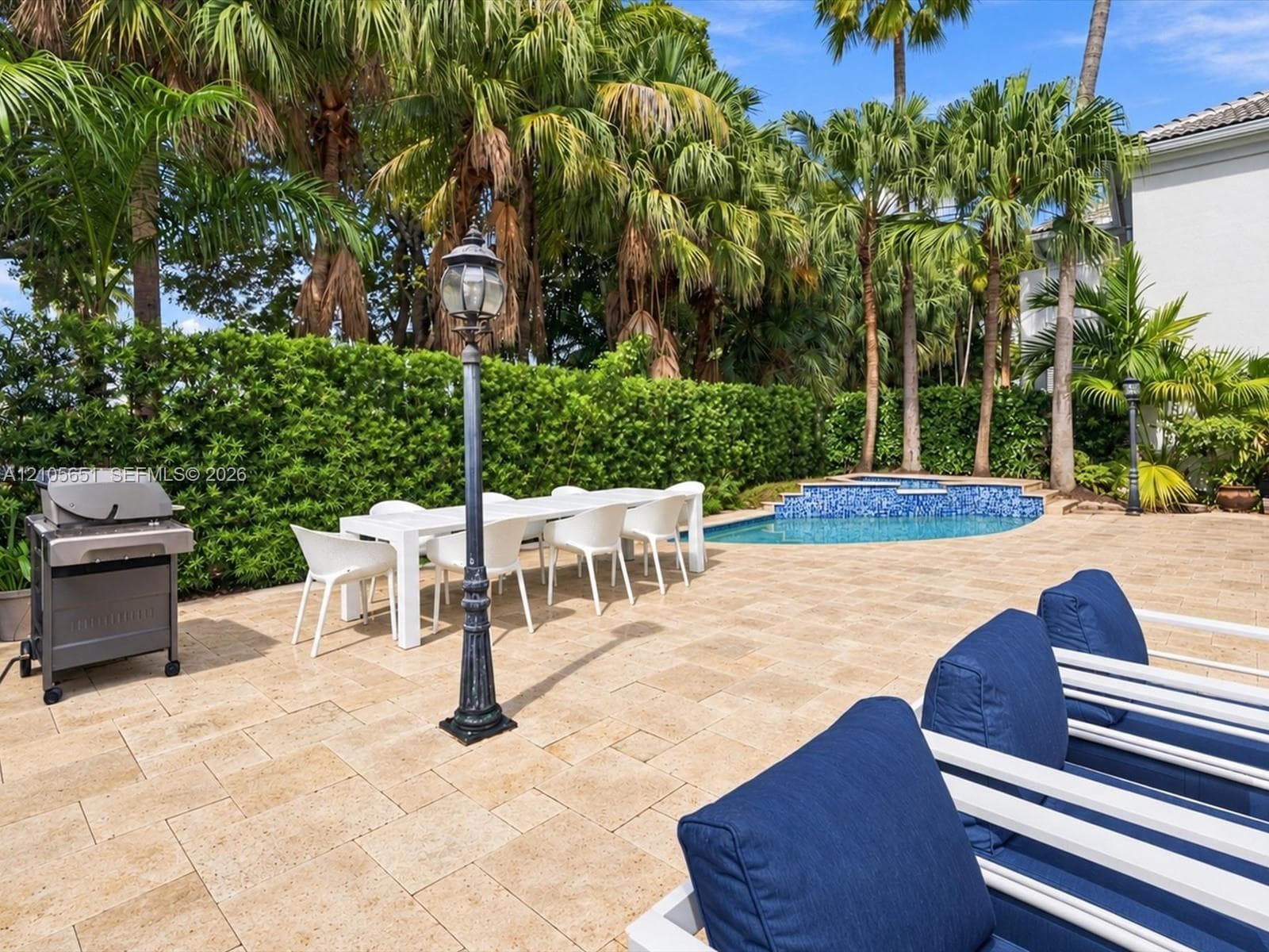 Outdoor living area featuring a stone-paver patio, a pool with a tile-accented spa, and perimeter hedging