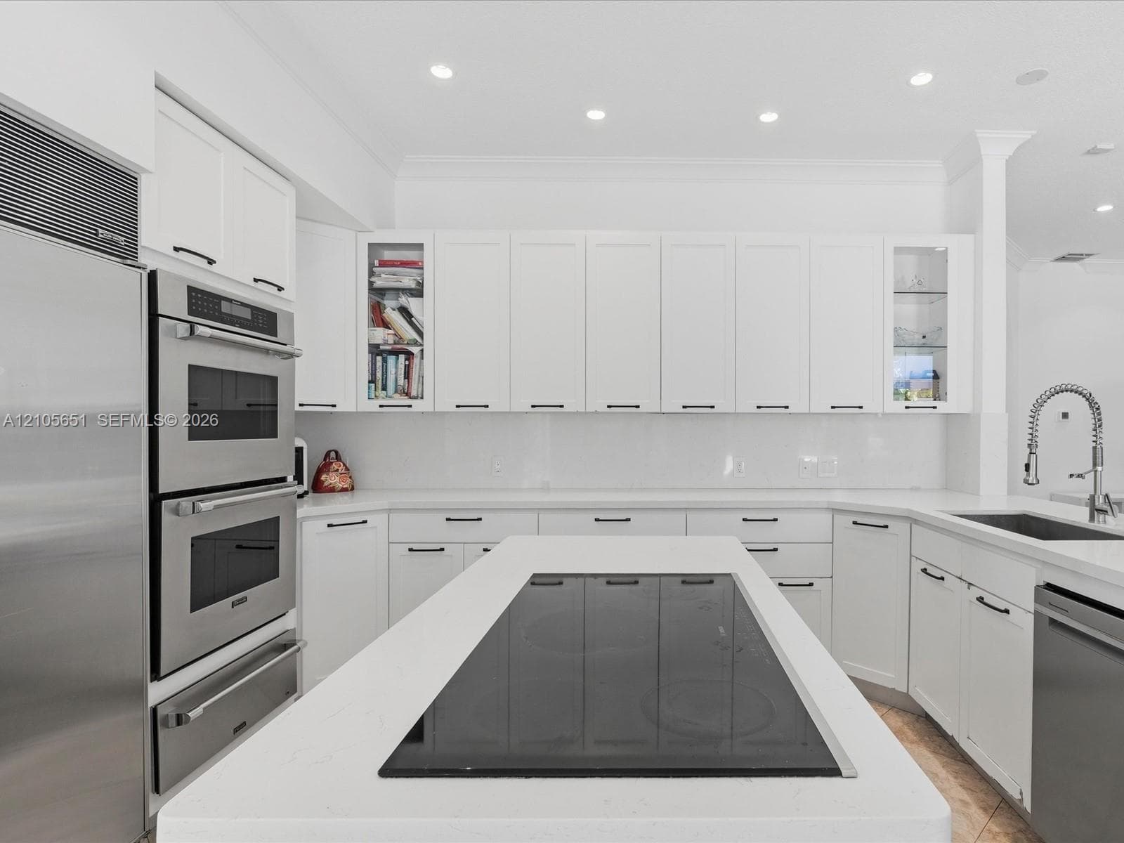 Kitchen featuring white cabinetry with glass-front display panels, quartz countertops, a central island with an integrated cooktop, double wall ovens, and a gooseneck faucet
