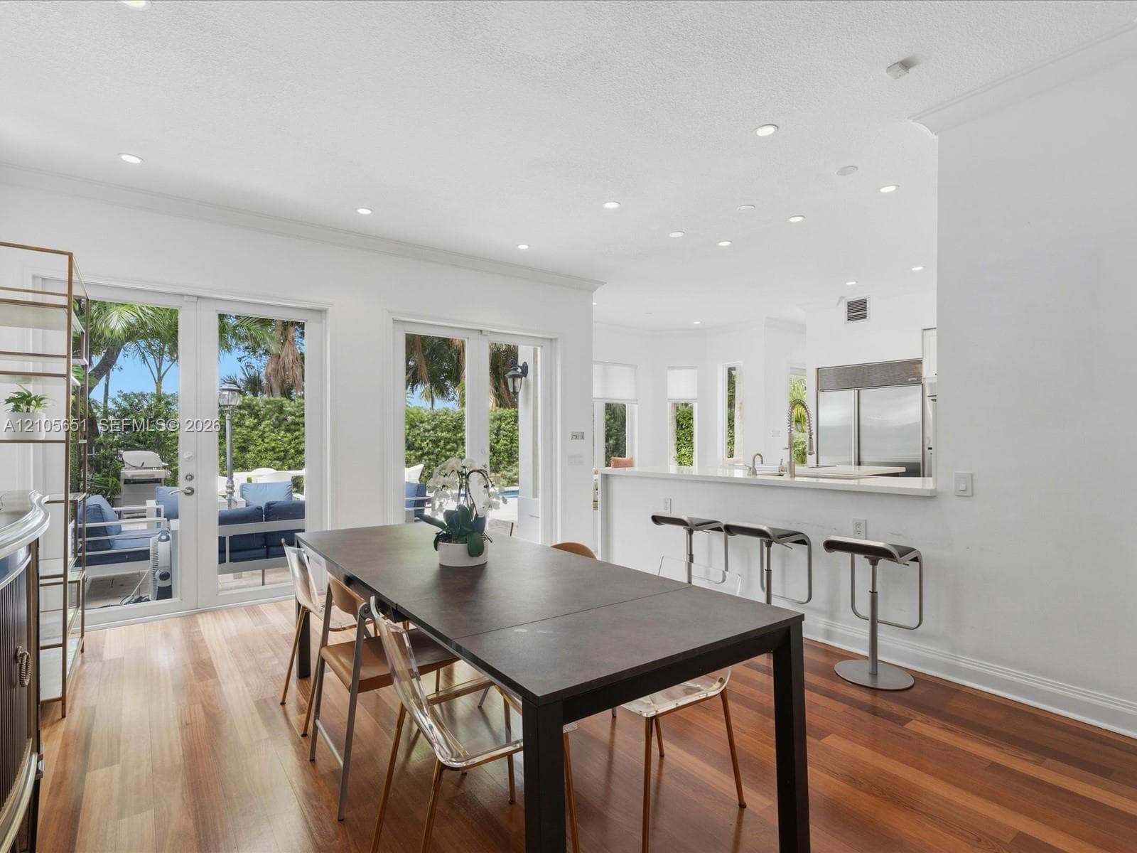 Open-concept dining area featuring wood-finish flooring, recessed lighting, breakfast bar with stone-finish countertop, and dual glass-panel doors