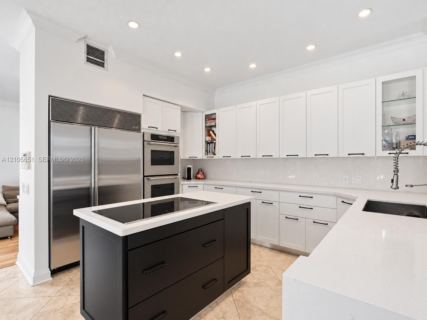 Kitchen featuring white shaker-style cabinetry, contrasting black center island, built-in stainless steel double wall oven, integrated refrigerator, and solid-surface countertops