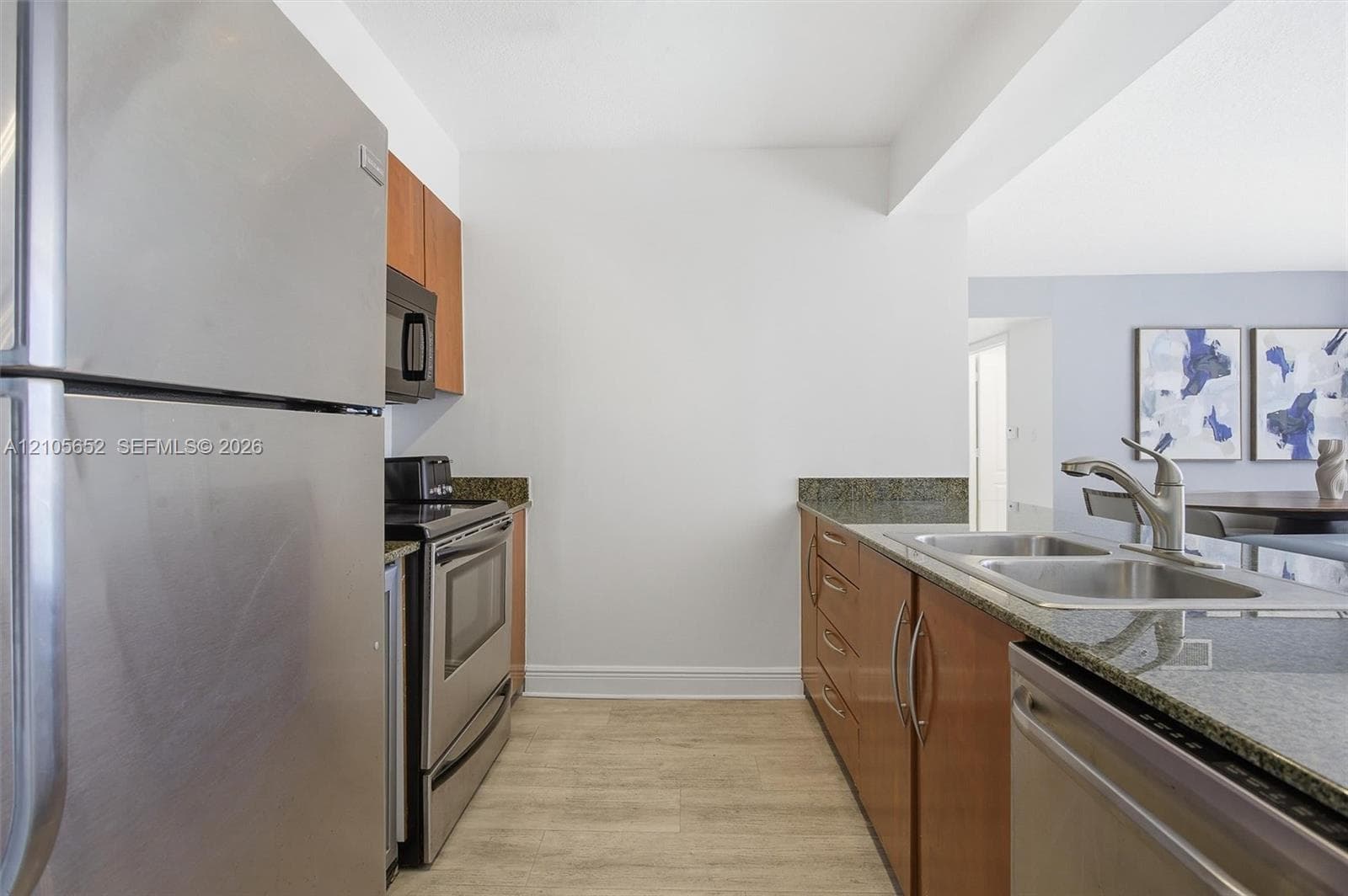 Kitchen featuring stainless steel appliances, stone countertops, wood-finish cabinetry, and a double-basin undermount sink