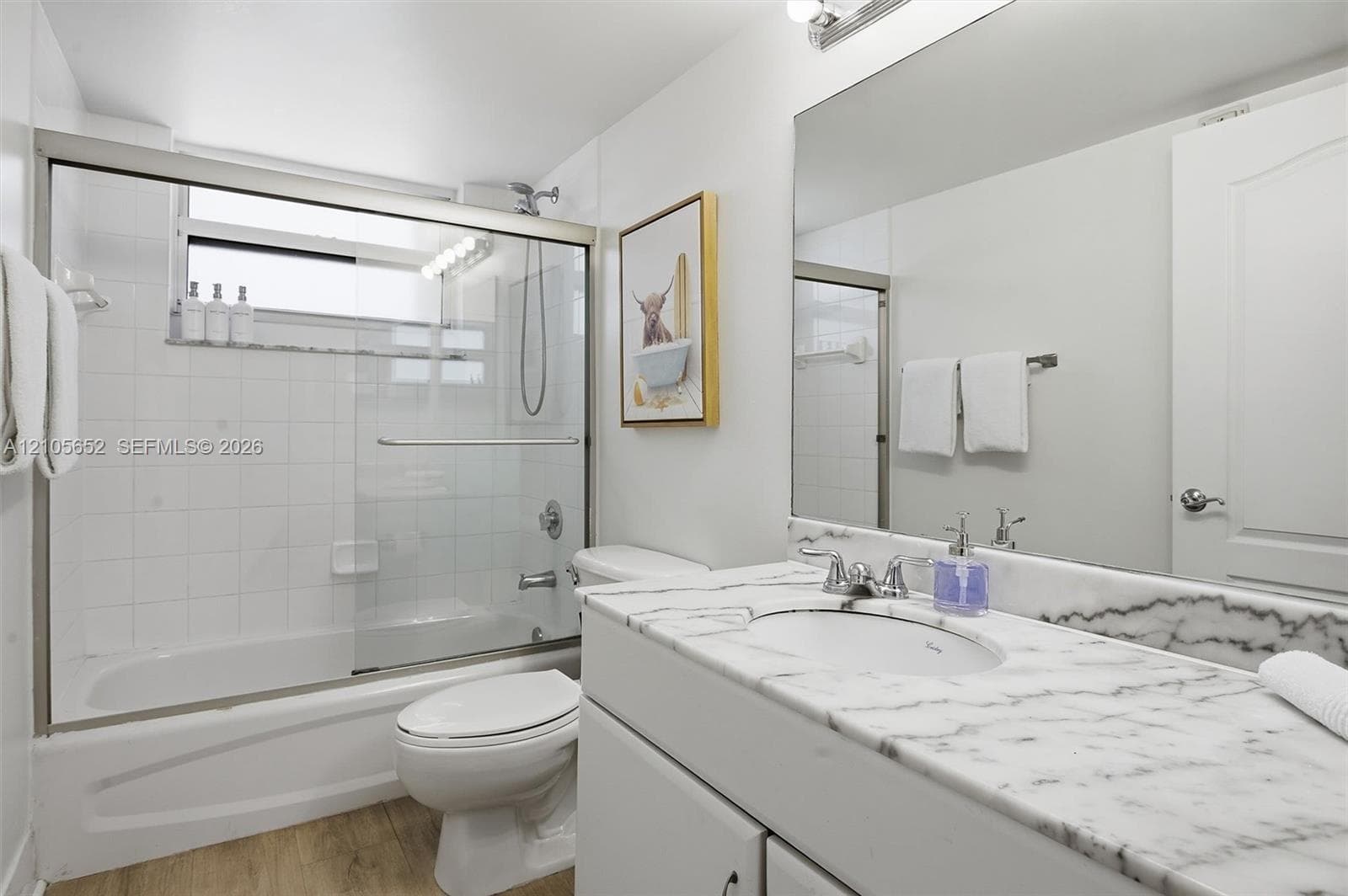 Bathroom featuring a vanity with a natural stone countertop, undermount sink, full-width vanity mirror, and a shower-tub combination with a sliding glass door and tiled surround