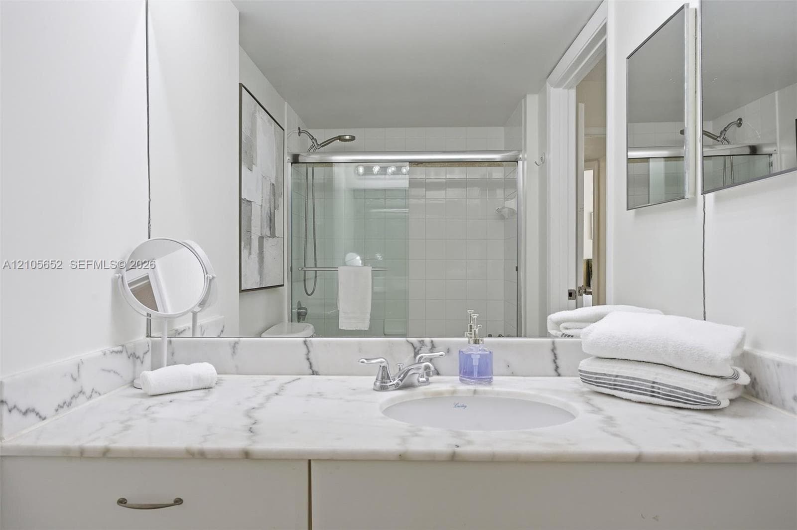 Bathroom featuring a stone vanity top with an integrated oval sink, polished chrome faucet, full-width mirror, and a walk-in shower with tiled surround and sliding glass doors