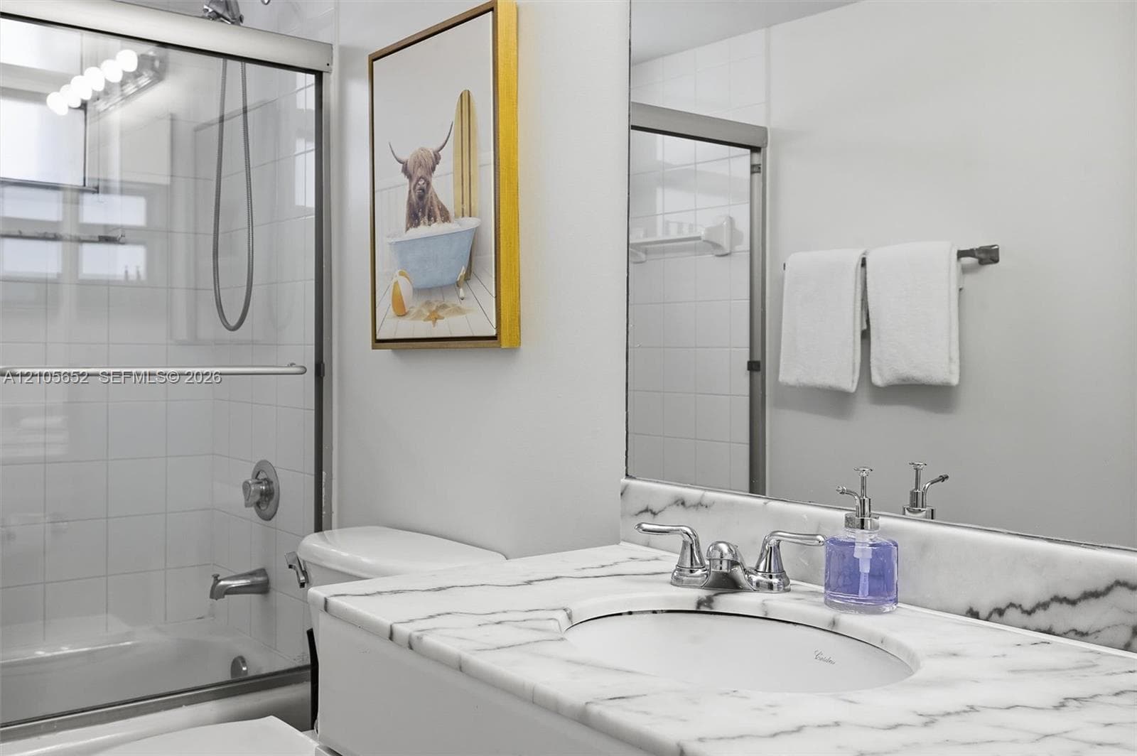 Bathroom featuring a vanity with a stone-surface countertop, an oval under-mount sink, a polished chrome faucet, a full-width mirror, and a tub-shower combination with a sliding glass enclosure and wall-mounted plumbing fixtures