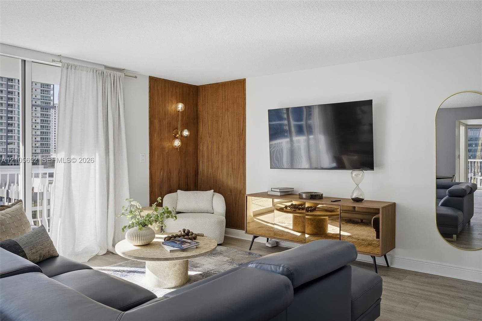 Living space featuring wood-finish flooring, floor-to-ceiling glass sliding doors, wood-panel accent wall, multi-globe wall-mounted light fixture, and oval wall-mounted mirror