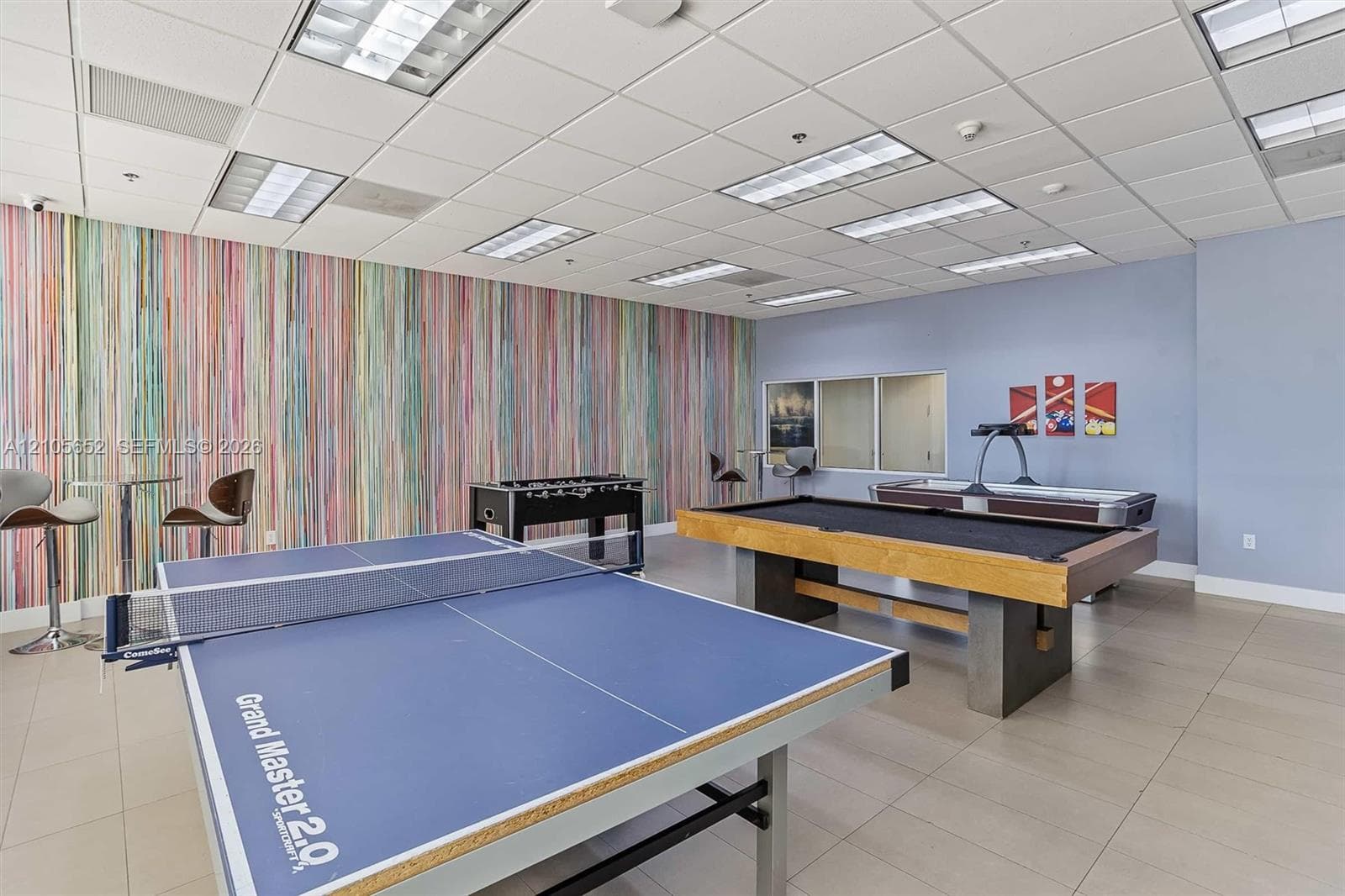 Spacious recreational area featuring a drop ceiling with integrated lighting, tile flooring, and a decorative multi-color vertical-stripe accent wall