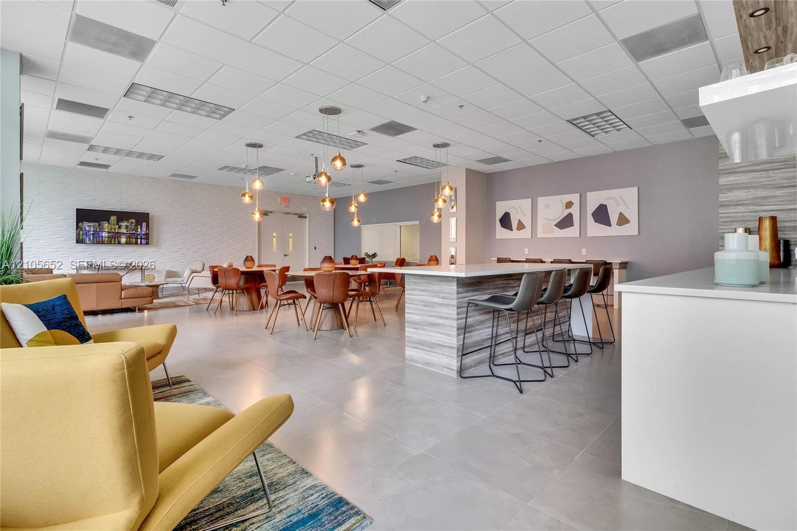 Large common area featuring tile flooring, a stone-finish kitchen island with seating, drop pendant lighting, and textured wall accents