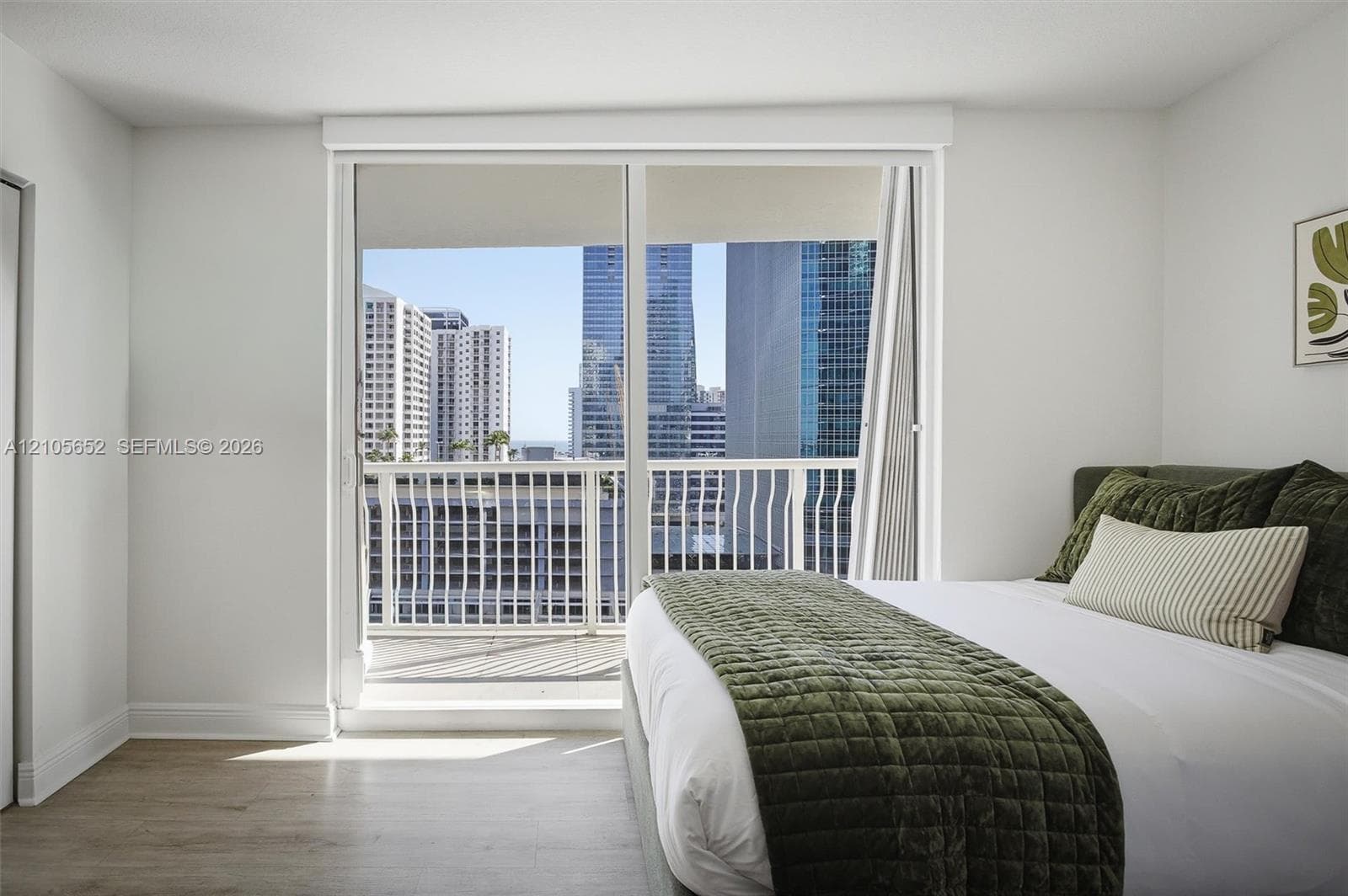 Floor-to-ceiling sliding glass door, private balcony with metal railing, and neutral wood-finish flooring