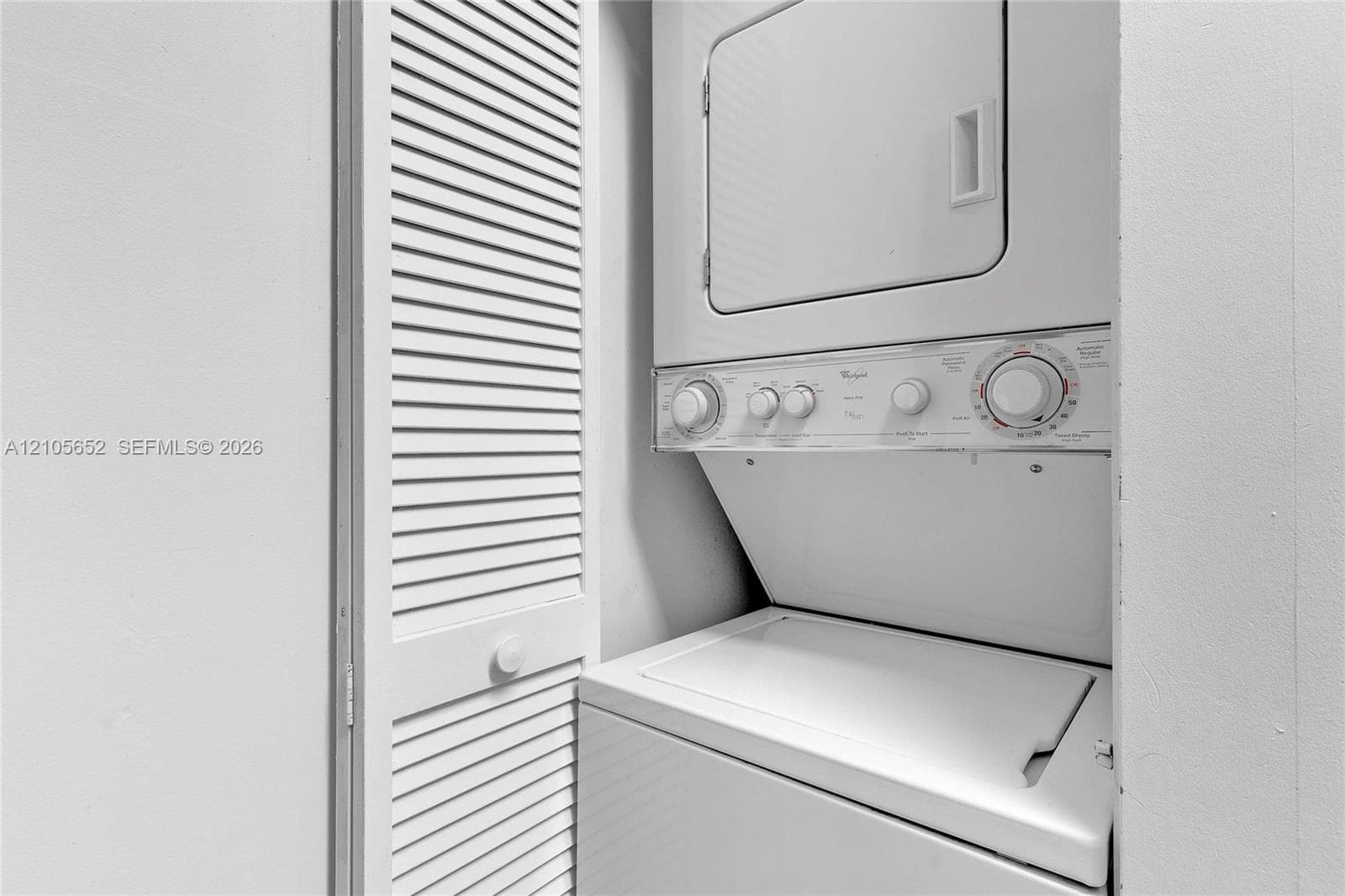 Stacked laundry unit with white finish, paired with a white louvered bifold closet door