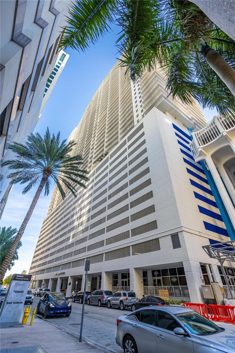 High-rise building exterior featuring a white concrete facade, vertical balcony columns, recessed window lines, and ground-level storefront glass