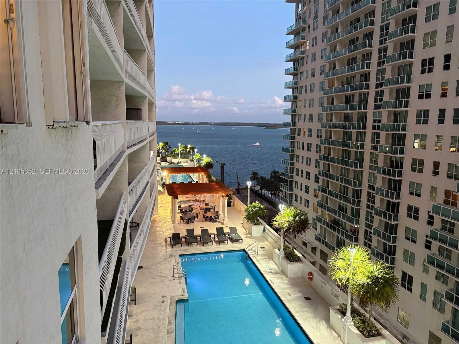 Outdoor swimming pool featuring stone deck surfacing, a covered pavilion, integrated landscape planters, and waterfront scenery