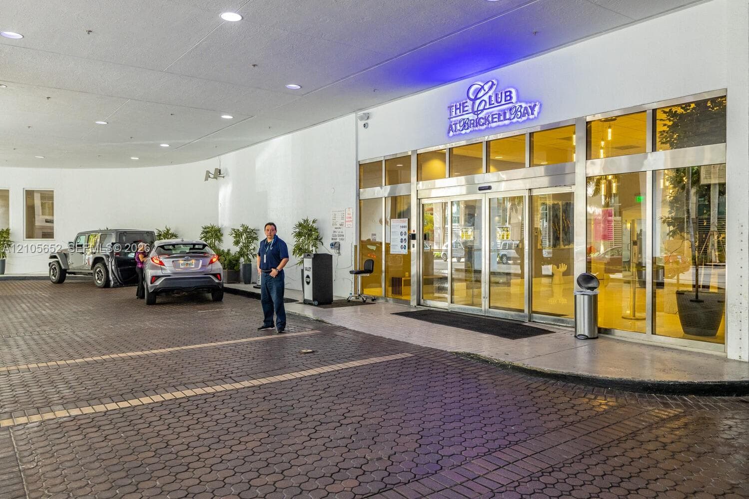 Covered motor court entrance featuring decorative brick paving, recessed ceiling lighting, and floor-to-ceiling glass panel doors