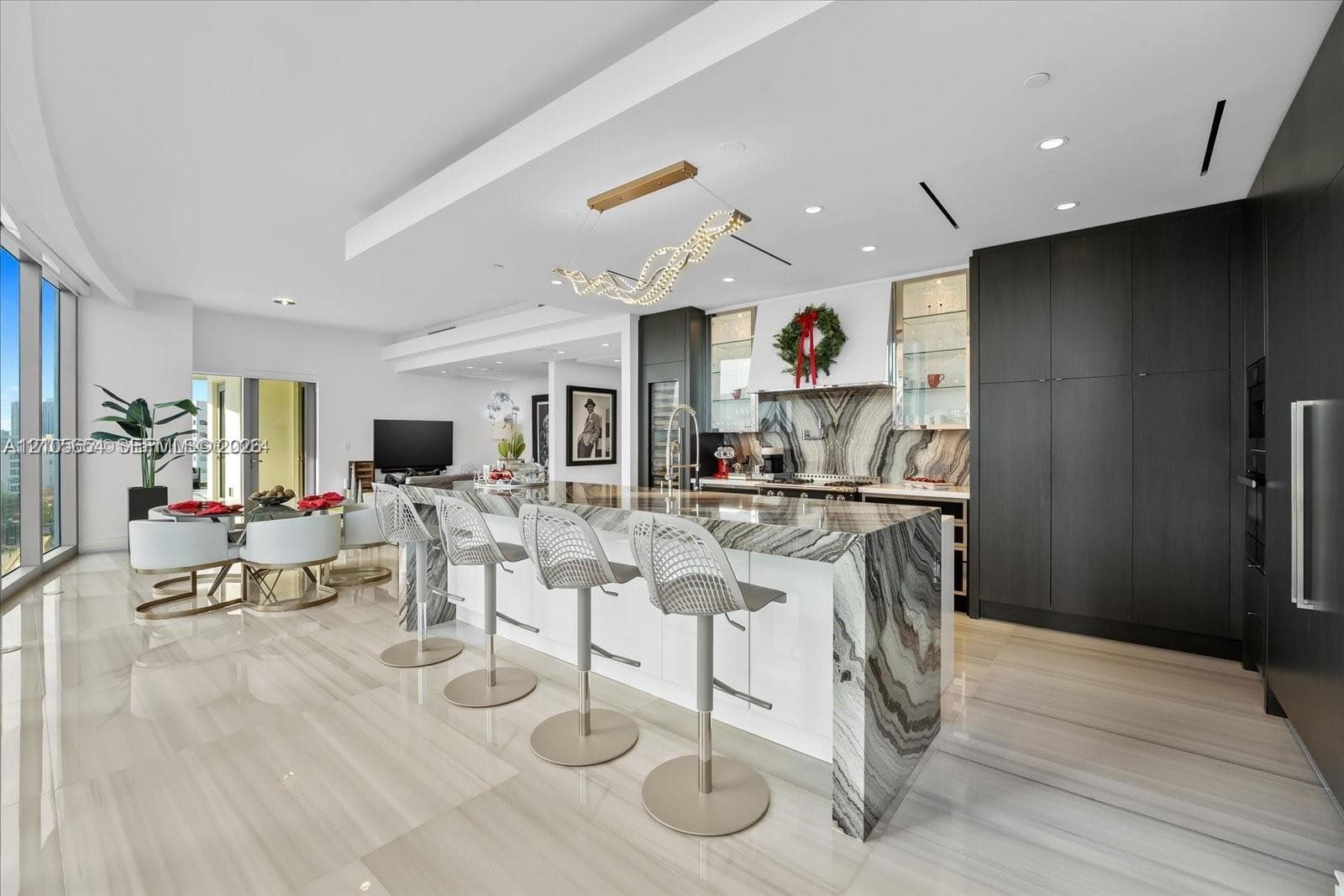 Open-concept kitchen featuring a waterfall-edge stone island, high-gloss flat-panel cabinetry, floor-to-ceiling dark cabinetry, large-format tile flooring, and custom contemporary lighting