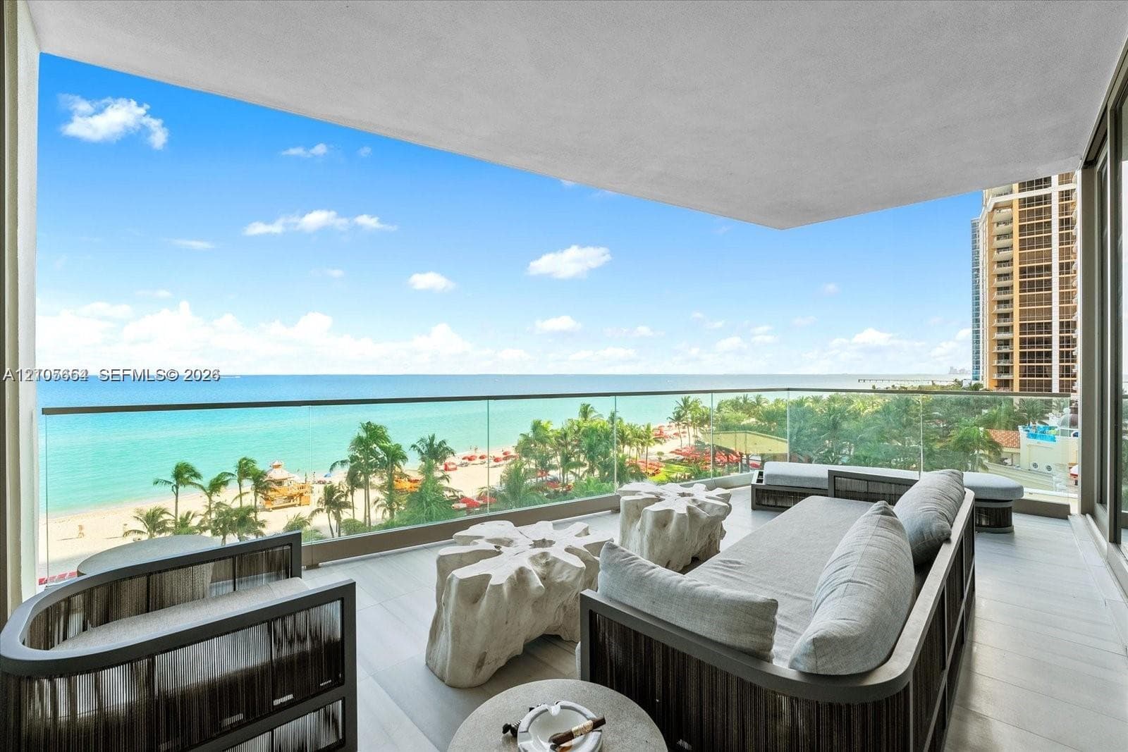Covered private balcony featuring large-format stone flooring and a seamless glass railing