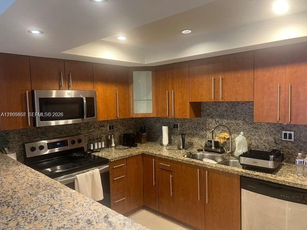 Kitchen featuring wood cabinetry, stone countertops, stainless steel microwave, recessed lighting, and a dual-basin sink with a gooseneck faucet