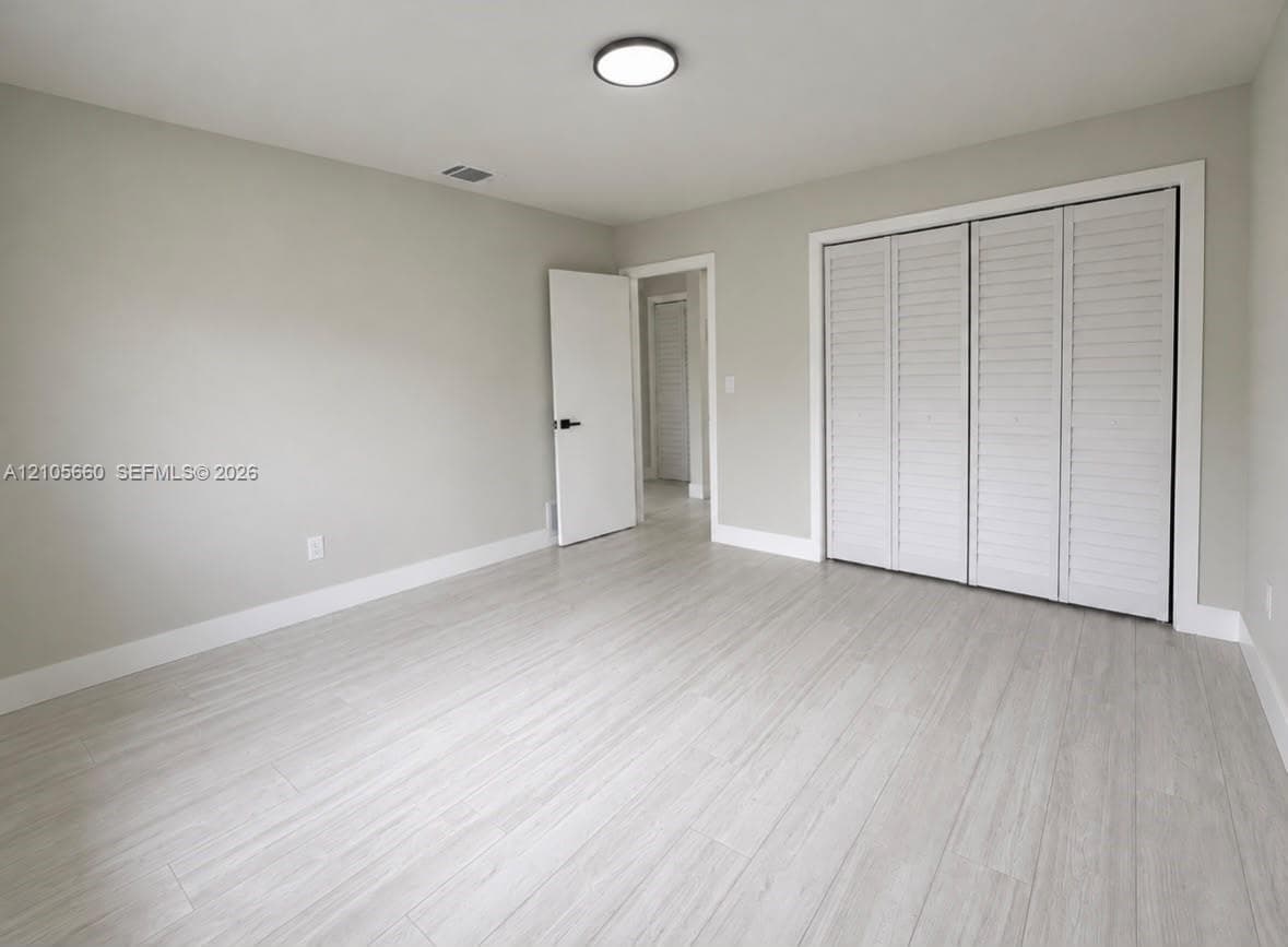 Neutral interior featuring wood-finish flooring, white louvered-style closet doors, and flush-mount ceiling lighting