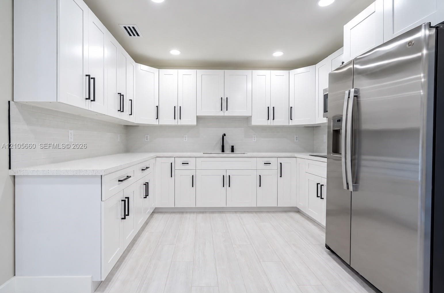 Kitchen featuring white shaker-style cabinetry, solid-surface countertops, horizontal tile backsplash, stainless steel refrigerator, and wood-finish flooring