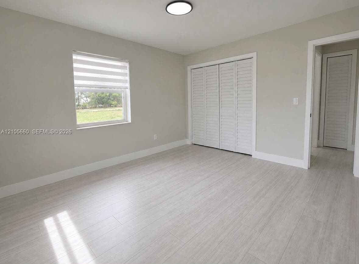 Interior space featuring wood-finish flooring, neutral wall paint, bi-fold closet doors, a flush-mount ceiling light fixture, and a window with a roller shade