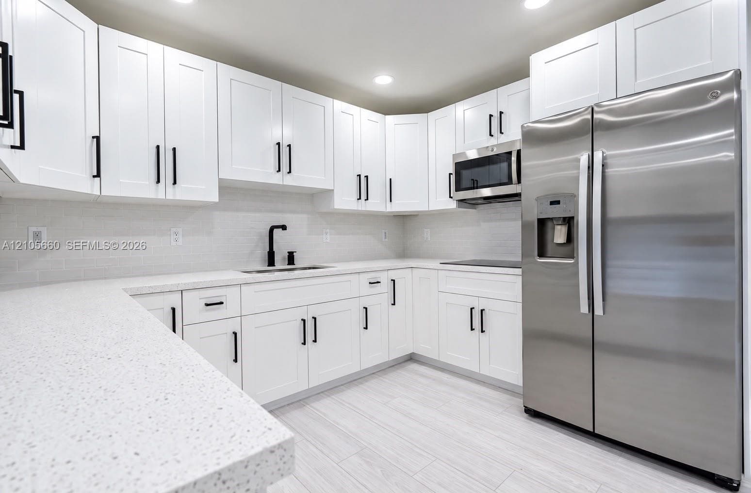 Kitchen featuring white shaker-style cabinetry, speckled light-toned countertops, subway tile backsplash, stainless steel appliances, and matte black hardware