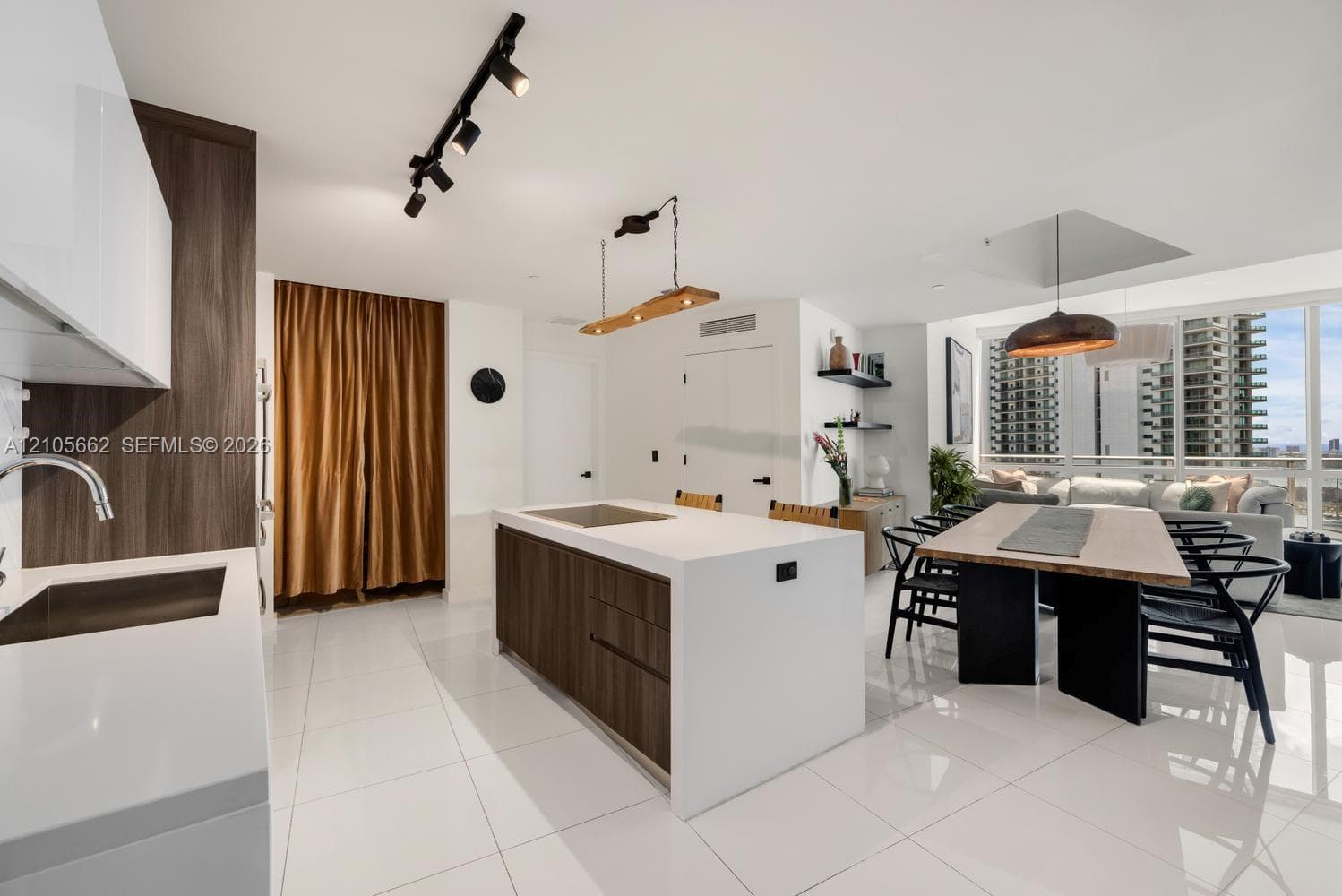 Kitchen featuring a central island with a solid-surface countertop and wood-finish cabinetry, gloss-finish white upper cabinets, track lighting, built-in shelving, and floor-to-ceiling windows