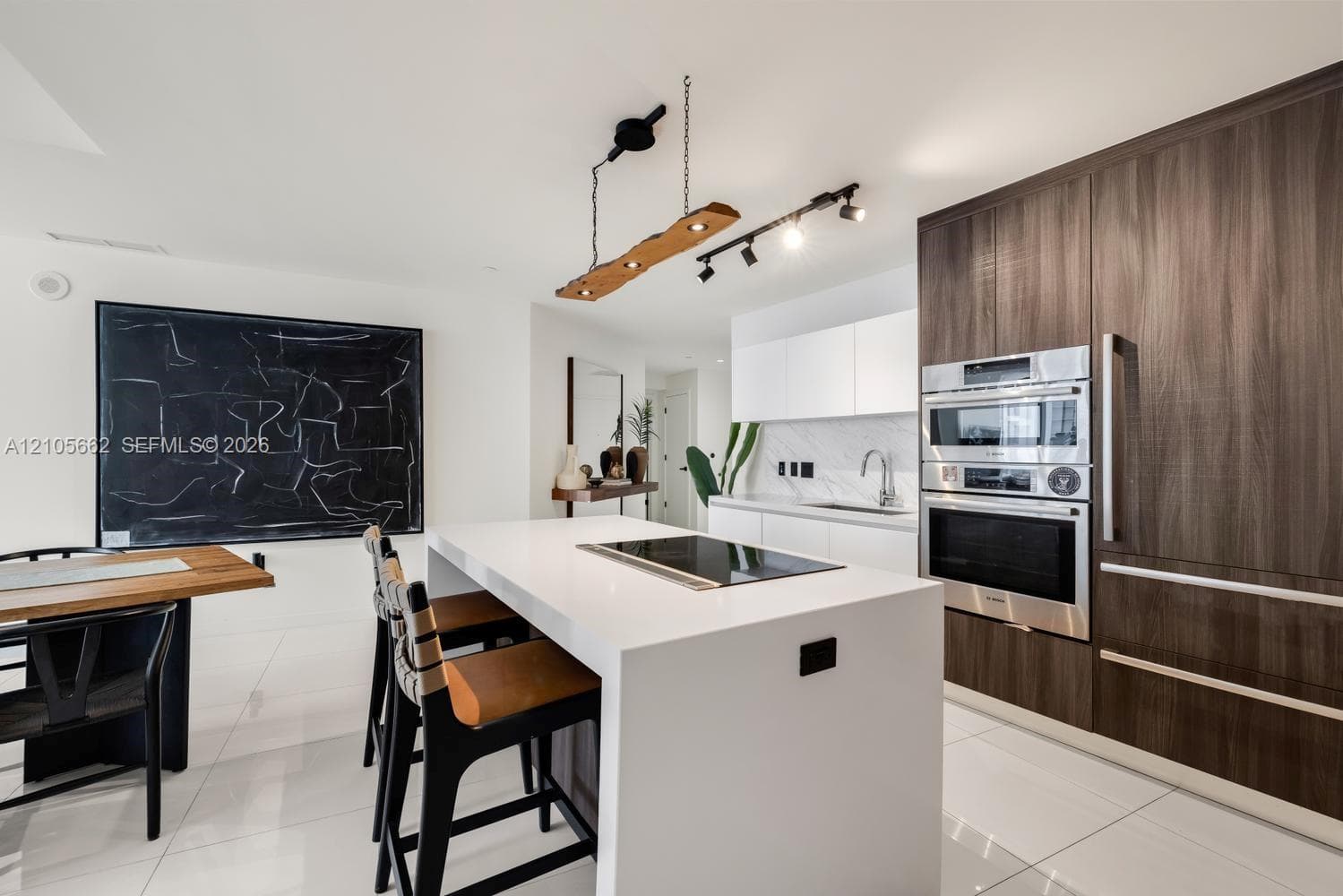 Kitchen featuring a center island with a built-in cooktop, stone-surfaced countertops, high-contrast wood-finish cabinetry, a stainless steel wall oven and microwave, and large-format tile flooring
