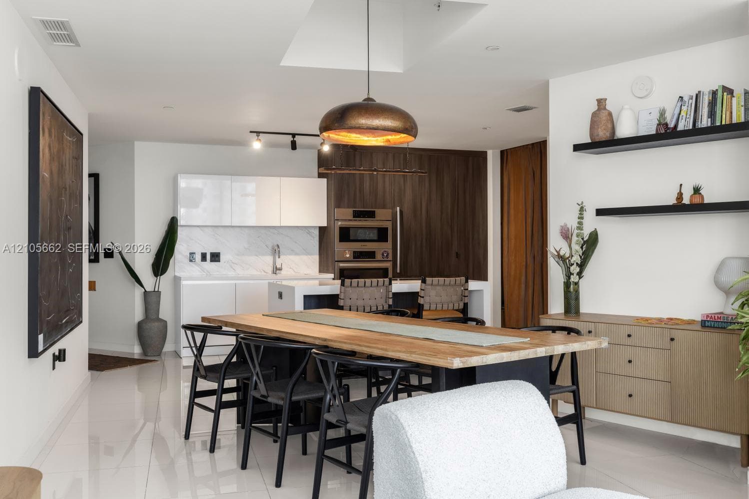 Kitchen featuring high-gloss cabinetry, stone-patterned backsplash, built-in double ovens, large center island, and overhead skylight